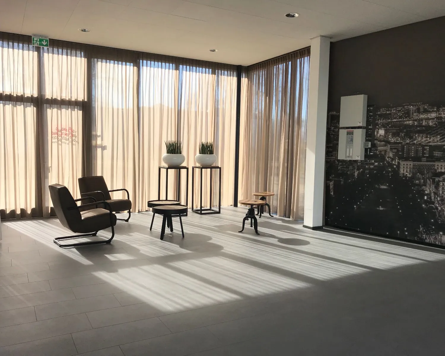 Zonnige wachtruimte met moderne stoelen, planten in witte potten en lange beige gordijnen.