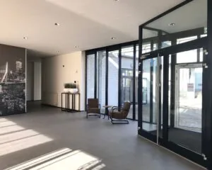 Moderne, lichte entreehal met glazen deuren, twee stoelen en een grote zwart-witfoto van de skyline van Rotterdam.
