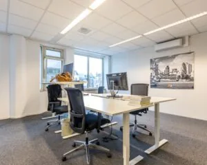 Modern kantoor met werkplekken, bureaustoelen, computers en een zwart-witfoto van Londen aan de muur.