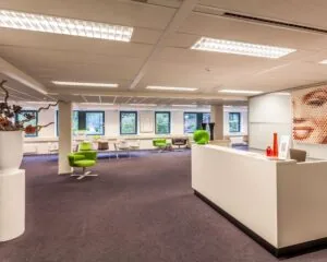 Moderne kantoorruimte met een receptiebalie, kleurrijke zitplaatsen en grote ramen die daglicht binnenlaten.