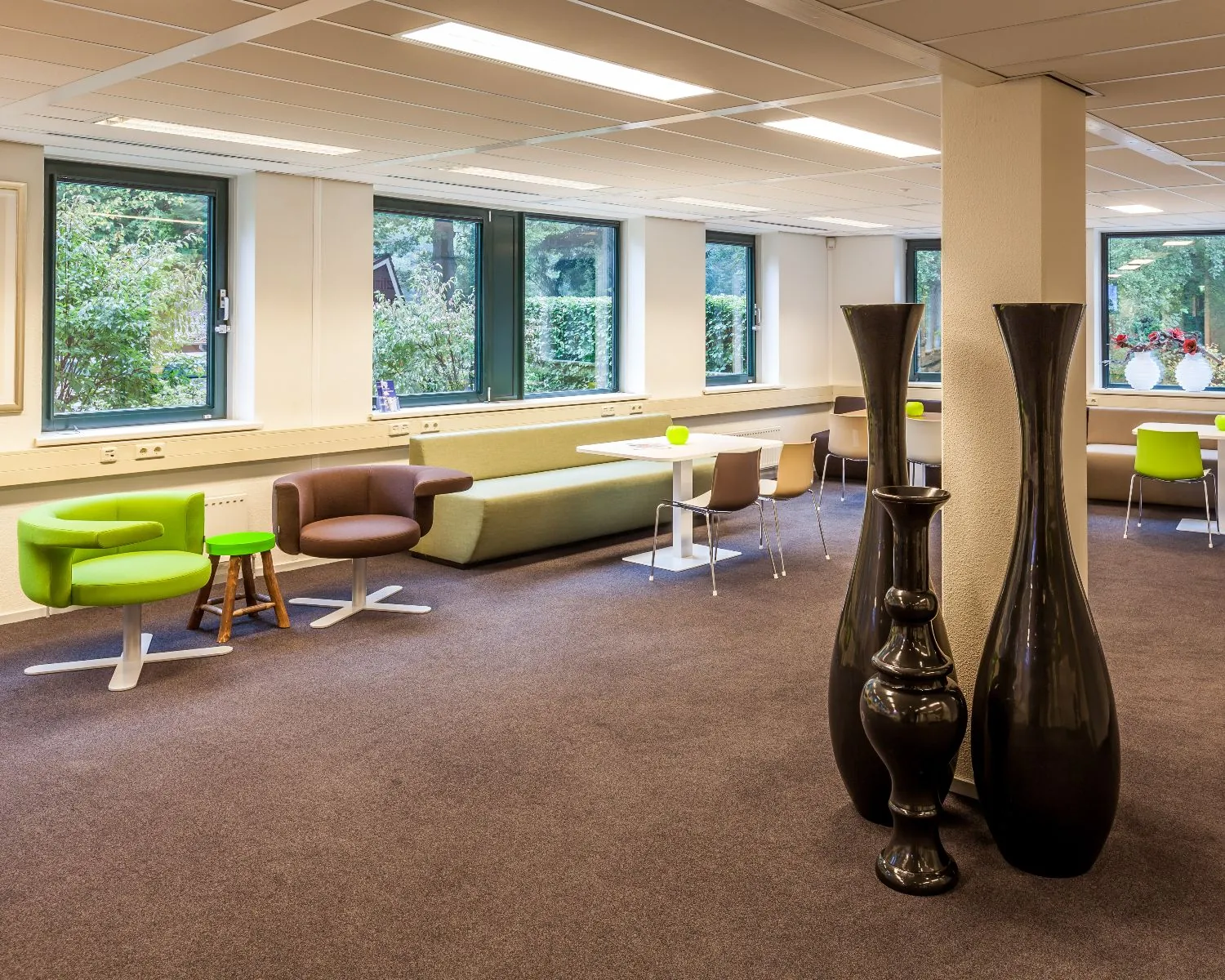 Moderne en kleurrijke zithoek met designstoelen, tafels en grote vazen in een open, licht interieur.