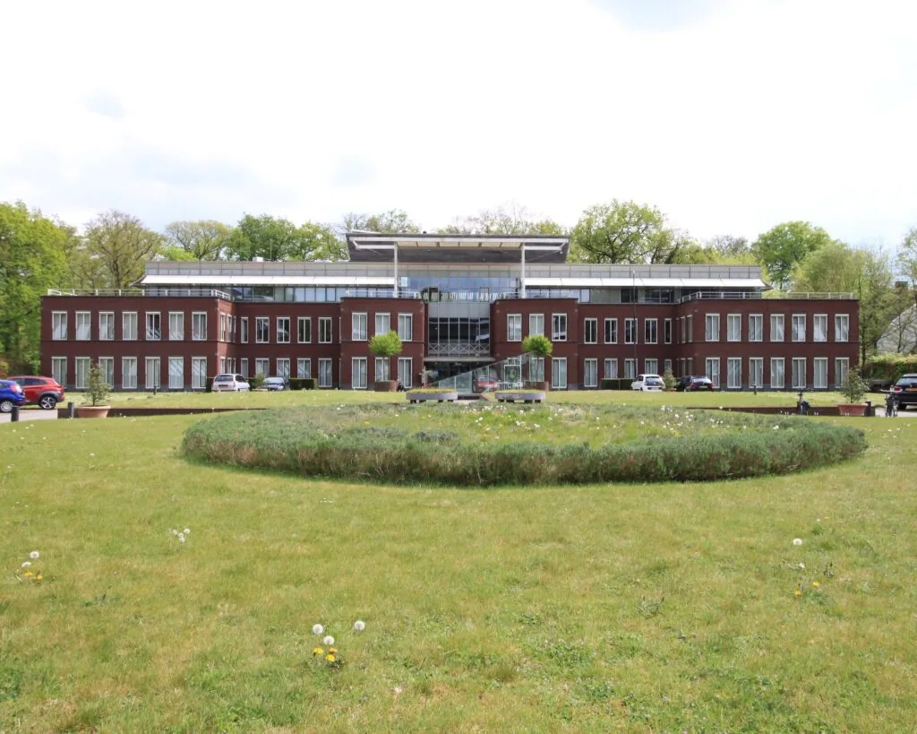 Modern kantoorgebouw met grote ramen en een ronde bloementuin op de voorgrond.