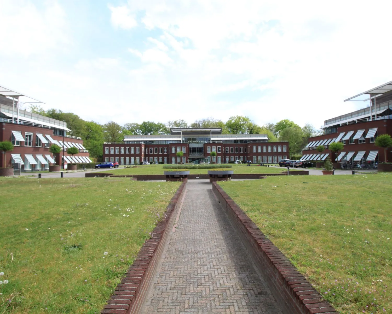 Modern kantoorgebouw met symmetrische architectuur en groene gazons, gezien vanaf een centrale looproute.