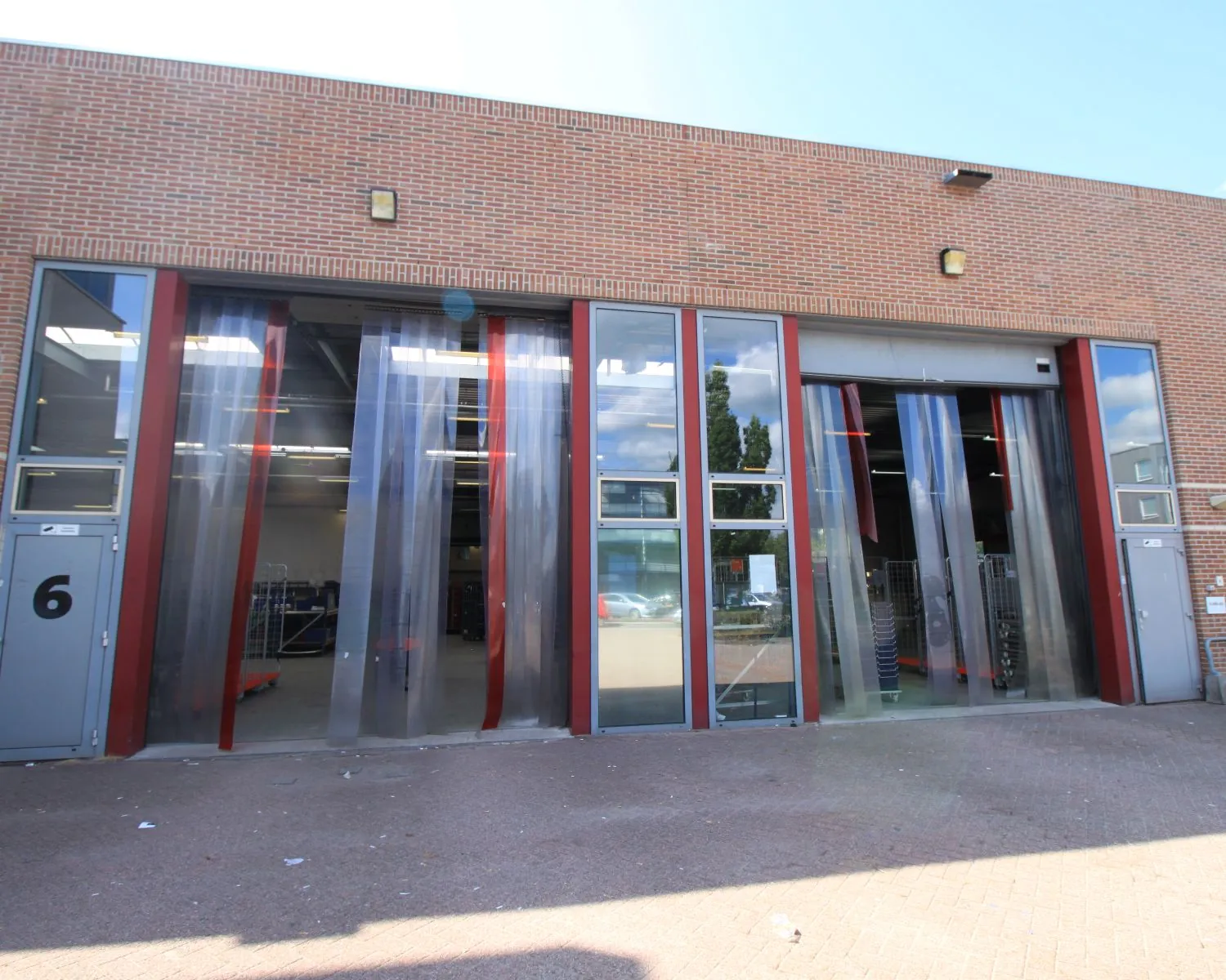 Ingang van een magazijn met transparante plastic strokengordijnen en bakwagens binnenin.