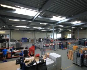 Overzicht van een ruime, goed georganiseerde loods met werkstations, medewerkers en stapels verzenddozen.