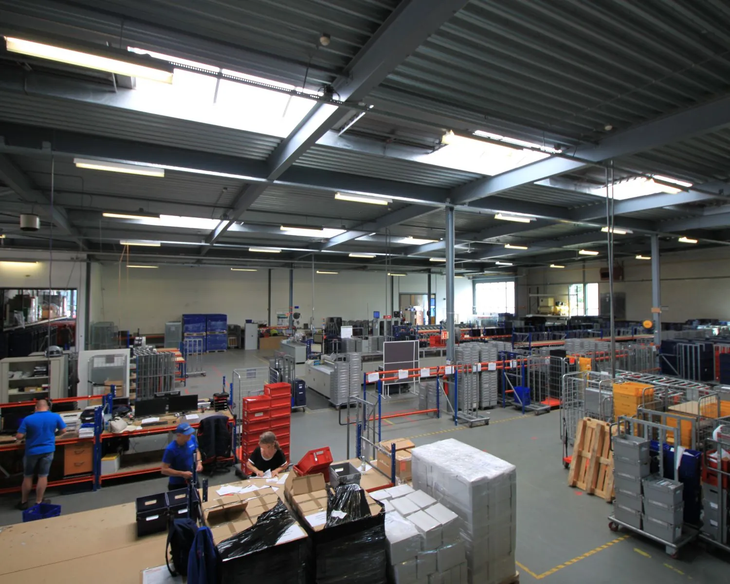 Overzicht van een ruime, goed georganiseerde loods met werkstations, medewerkers en stapels verzenddozen.