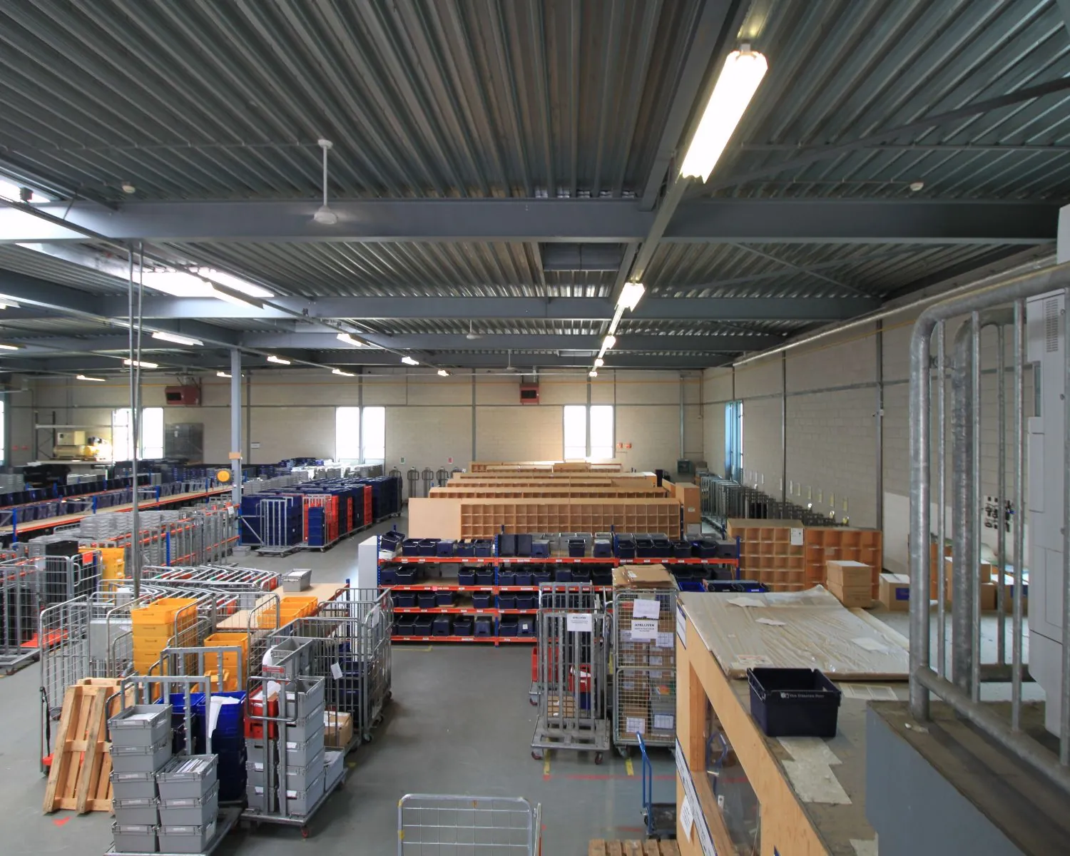 Ruime, goed verlichte opslagruimte met stellingen, rolcontainers en sorteervakken in een industriële loods.