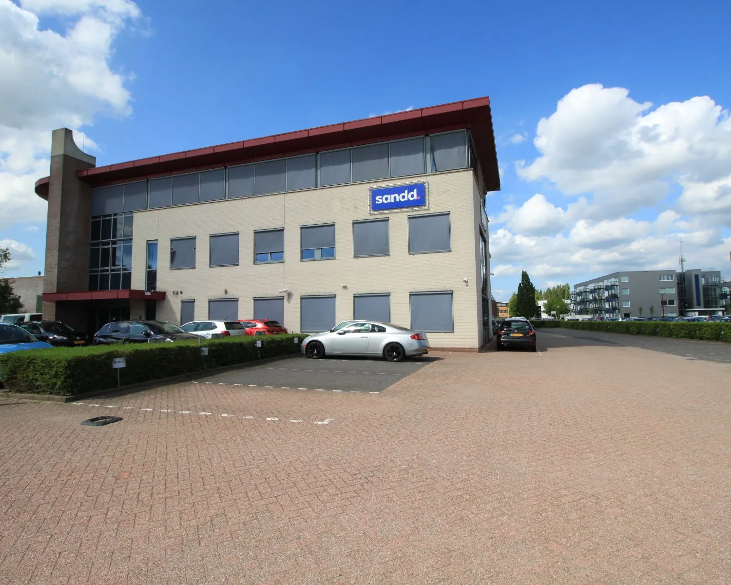 Kantoorgebouw van Sandd met parkeergelegenheid op een zonnige dag.