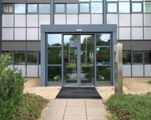Ingang van een modern kantoorgebouw met glazen deuren en een toegangszuil.