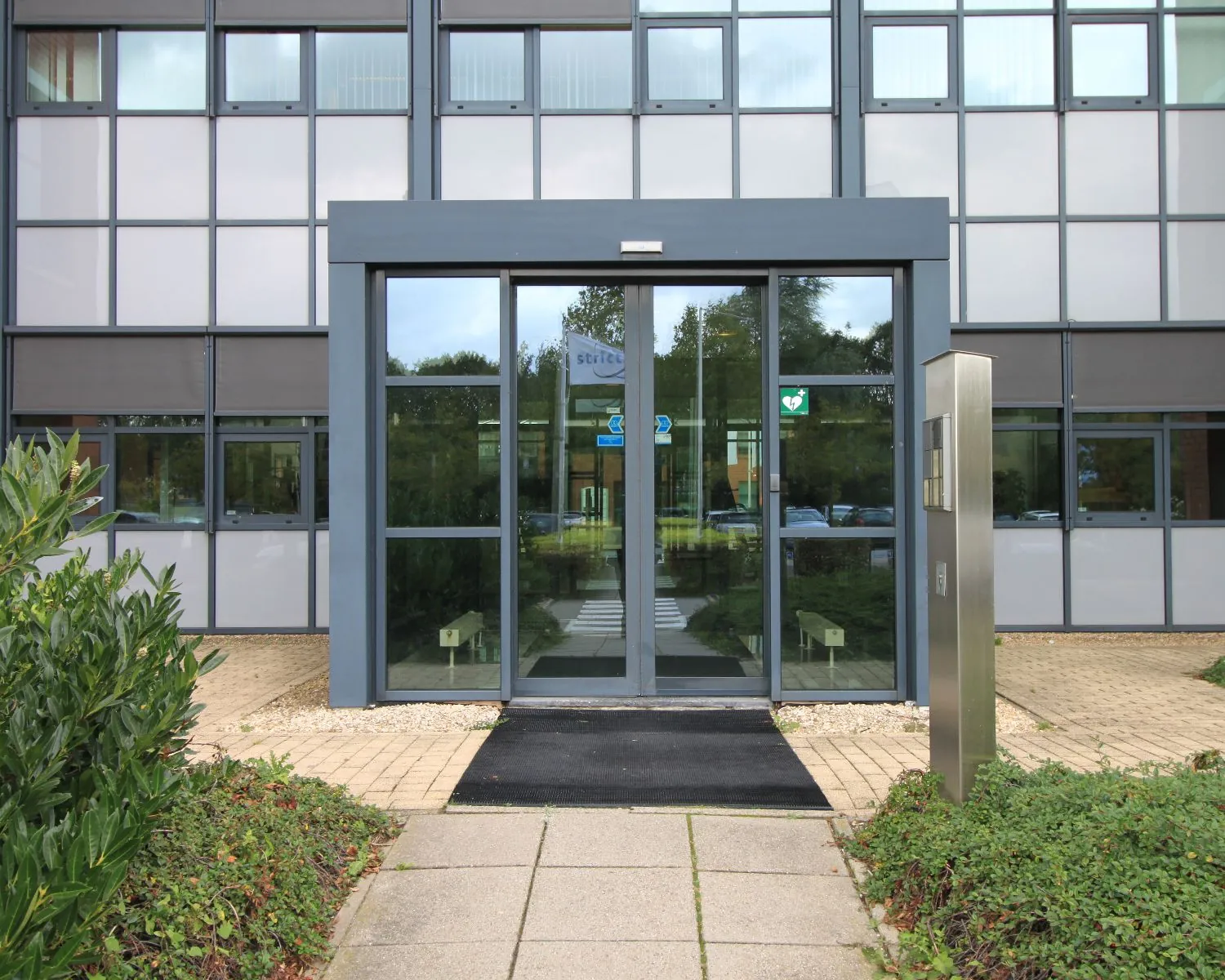 Ingang van een modern kantoorgebouw met glazen deuren en een toegangszuil.