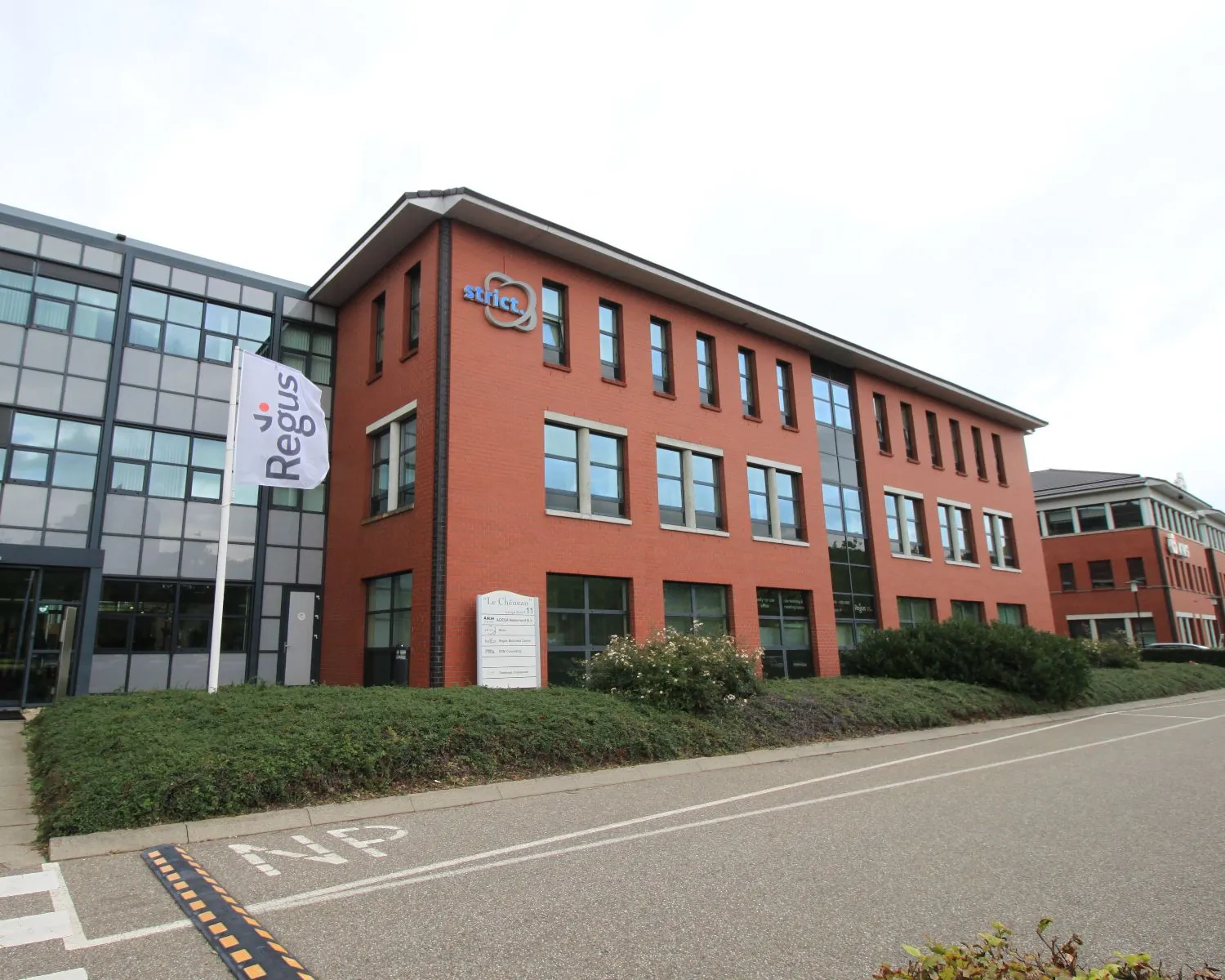 Kantoorgebouw met de logo's van Strict en Regus aan de gevel, gelegen aan een rustige weg.