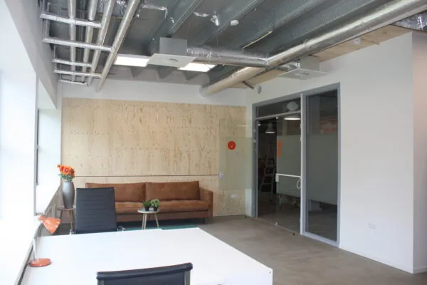 Modern kantoorinterieur met een leren bank, houten wandbekleding en zichtbaar plafond met ventilatiebuizen.