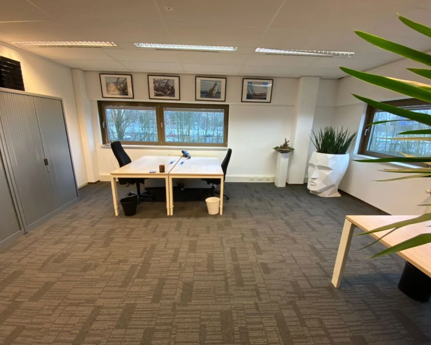 Modern kantoor met twee bureaus, kunst aan de muur en een opvallende plantenbak in de vorm van een gezicht.