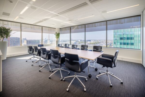 Een moderne vergaderruimte met grote ramen, een lange tafel en zwarte stoelen.