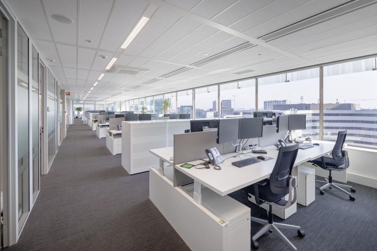 Een moderne, lichtovergoten kantoorruimte met rijen van lege bureaus en computers.