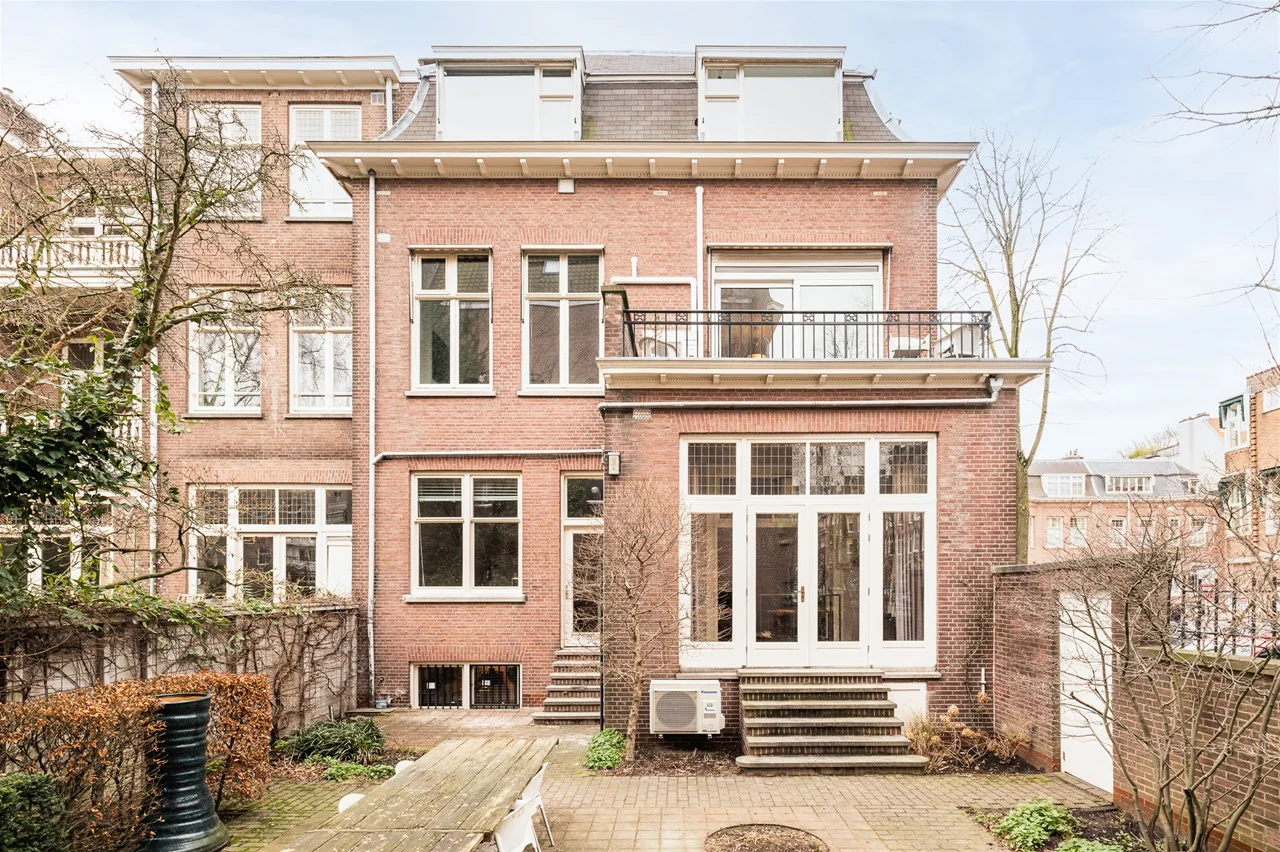 Achteraanzicht van een rood bakstenen herenhuis aan de Jacob Obrechtstraat 11 met grote ramen, openslaande deuren en een verzorgde stadstuin.