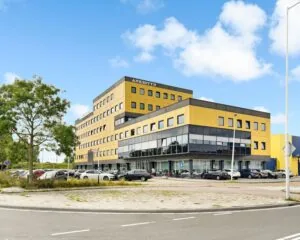 Modern geel kantoorgebouw genaamd Ankostyn aan de Joan Muyskenweg in Amsterdam met parkeergelegenheid ervoor.