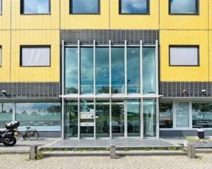 Glazen entree van een modern kantoorgebouw aan de Joan Muyskenweg 40-146 in Amsterdam met gele en zwarte gevel.