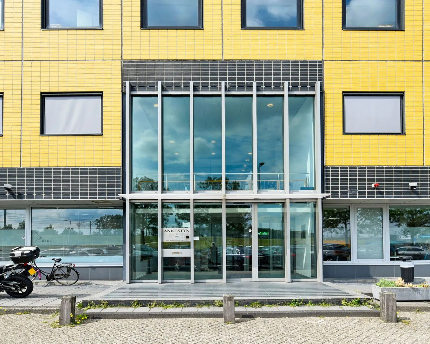Glazen entree van een modern kantoorgebouw aan de Joan Muyskenweg 40-146 in Amsterdam met gele en zwarte gevel.