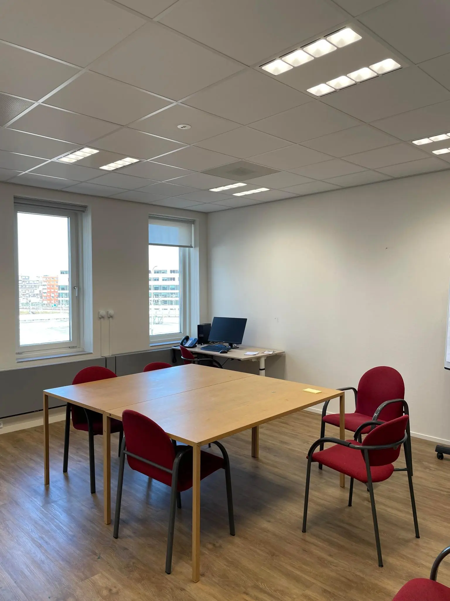 Kantoorruimte aan de Johan Cruijff Boulevard met een vergadertafel, rode stoelen en een bureau met computer.
