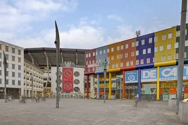 Kleurrijk kantoorgebouw en winkelpand aan de Johan Cruijff Boulevard met zicht op de Johan Cruijff ArenA.