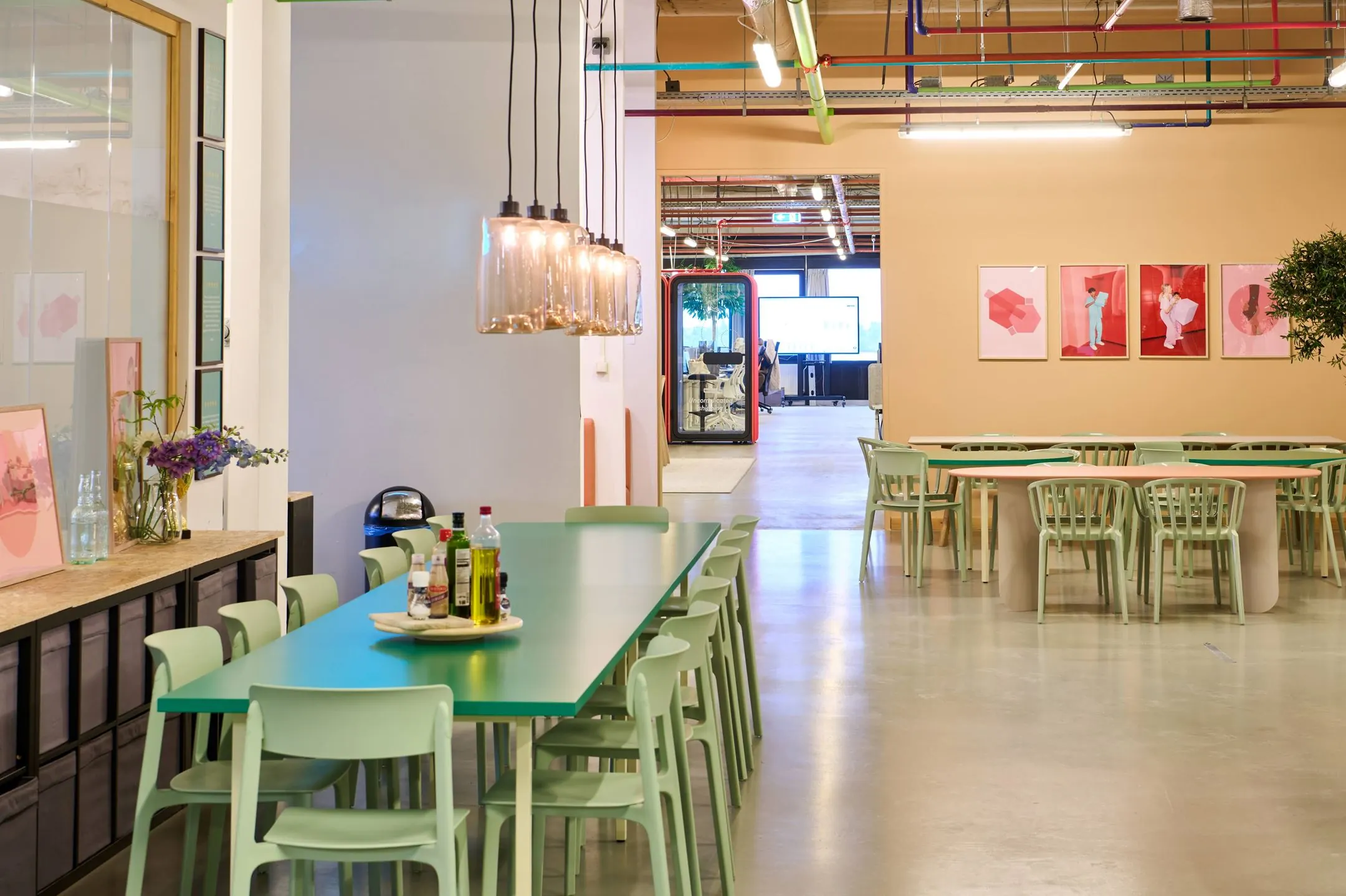 Kleurrijke en moderne kantine met mintgroene stoelen, lange tafels en glazen hanglampen in het kantoor aan de Johan Huizingalaan 763a.