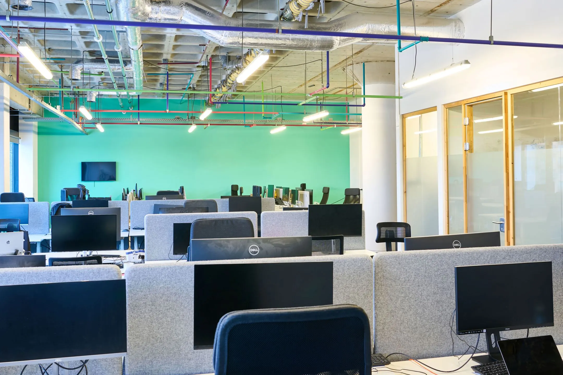 Moderne open kantoorruimte aan de Johan Huizingalaan 763a met grijze bureauschermen, meerdere computerschermen en een mintgroene muur.