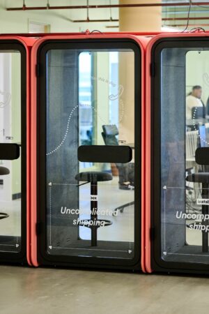 Twee rode telefooncabines met de tekst "Uncomplicated shipping" staan in een modern kantoor aan de Johan Huizingalaan 763a.