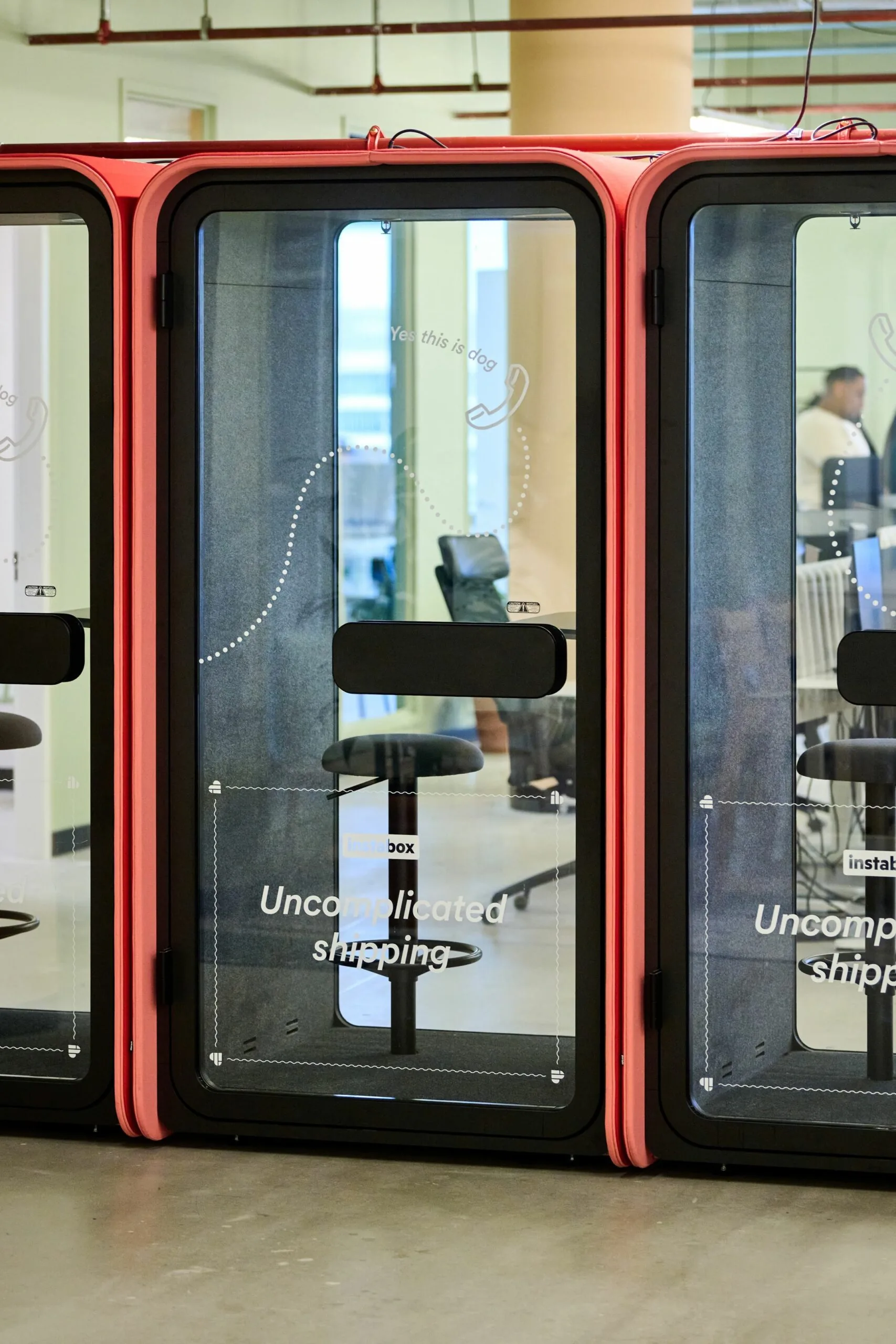 Twee rode telefooncabines met de tekst "Uncomplicated shipping" staan in een modern kantoor aan de Johan Huizingalaan 763a.