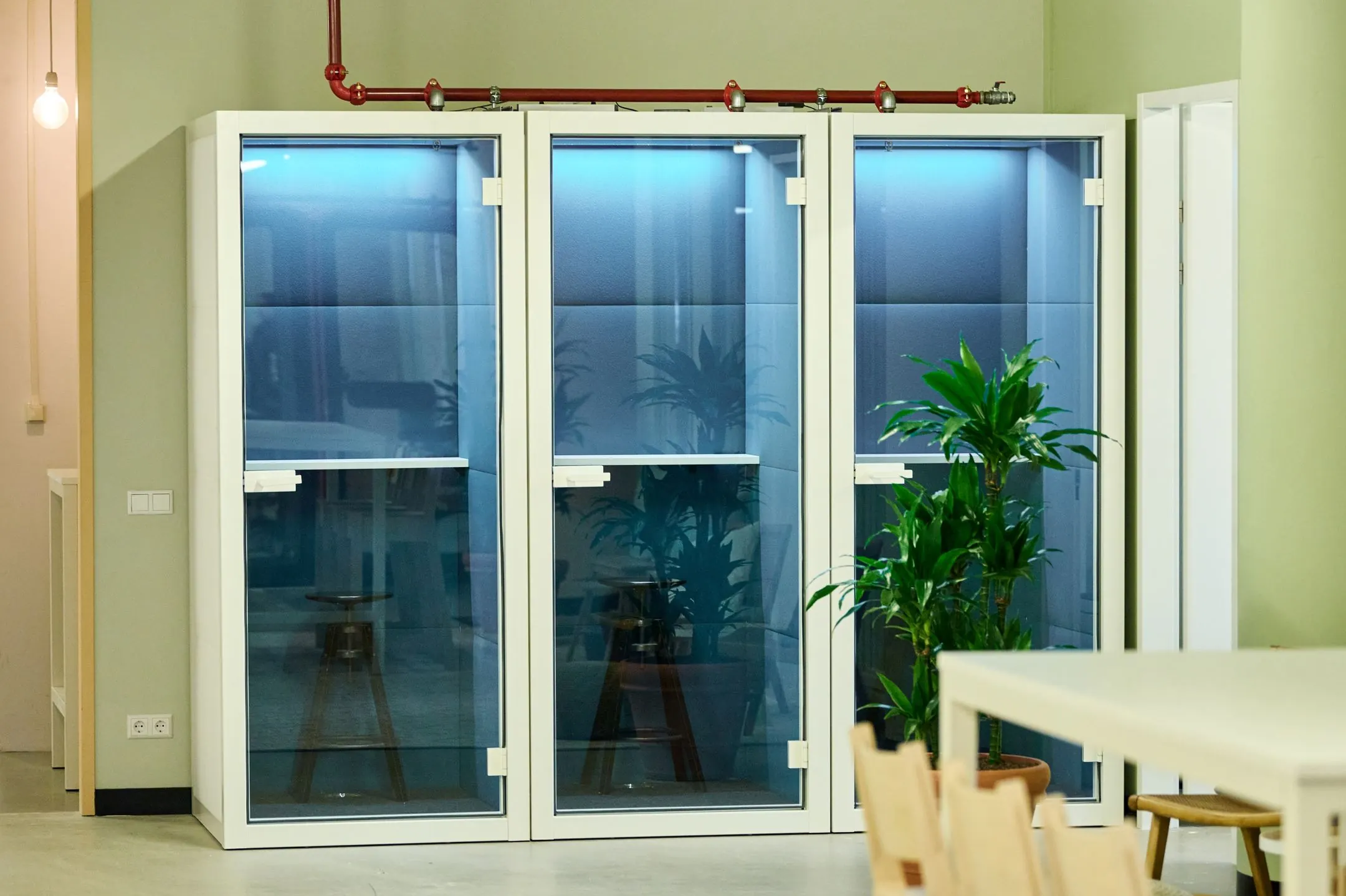 Drie glazen belcabines met blauwe verlichting en een plant ernaast in een modern kantoor aan de Johan Huizingalaan 763a.
