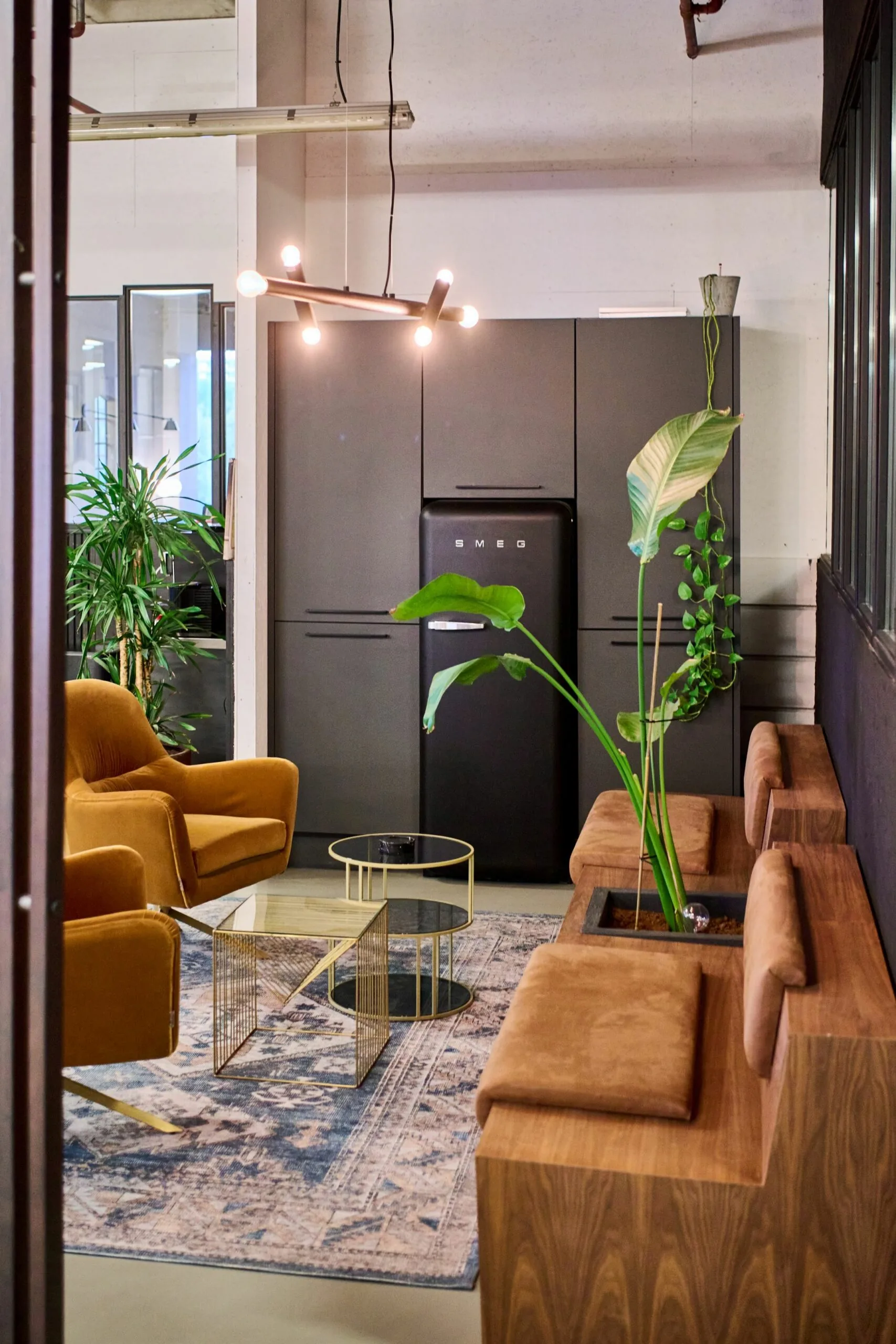 Modern ingerichte loungehoek bij Johan Huizingalaan 763a met fluwelen stoelen, designmeubels, planten en een zwarte Smeg-koelkast.