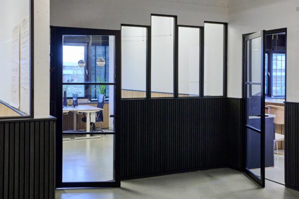 Moderne kantoorruimte aan de Johan Huizingalaan 763a met glazen wanden, zwarte kozijnen en zicht op een werkplek met bureaustoel en planten.