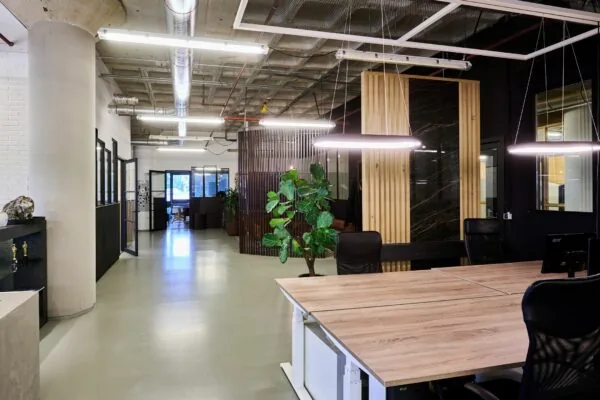 Modern kantoorinterieur aan de Johan Huizingalaan 763a met houten bureaus, industriële plafonddetails en een groene plant.