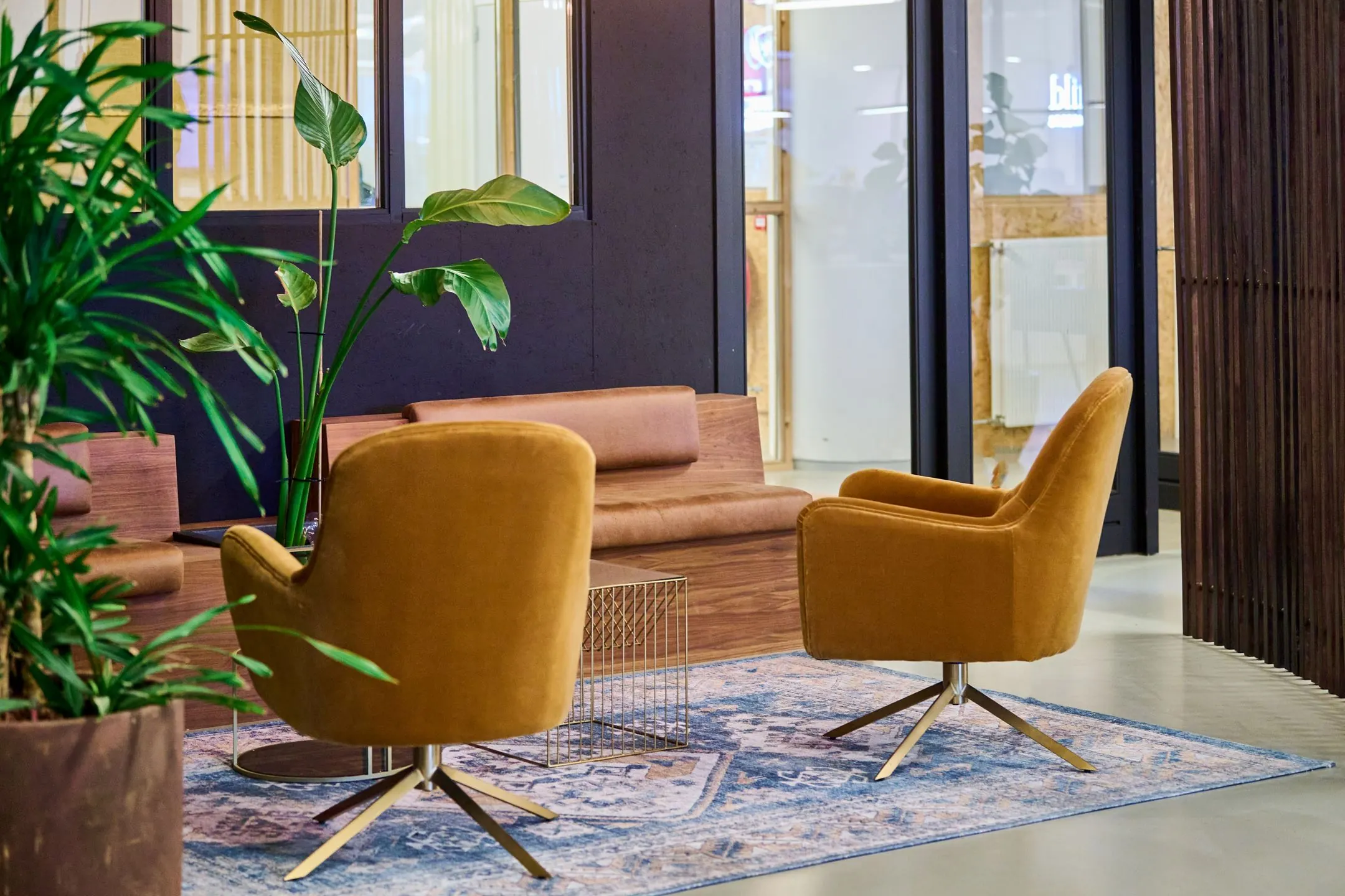 Moderne wachtruimte met okergele stoelen, een houten bank, blauwe vloerkleed en groene kamerplanten bij Johan Huizingalaan 763a.