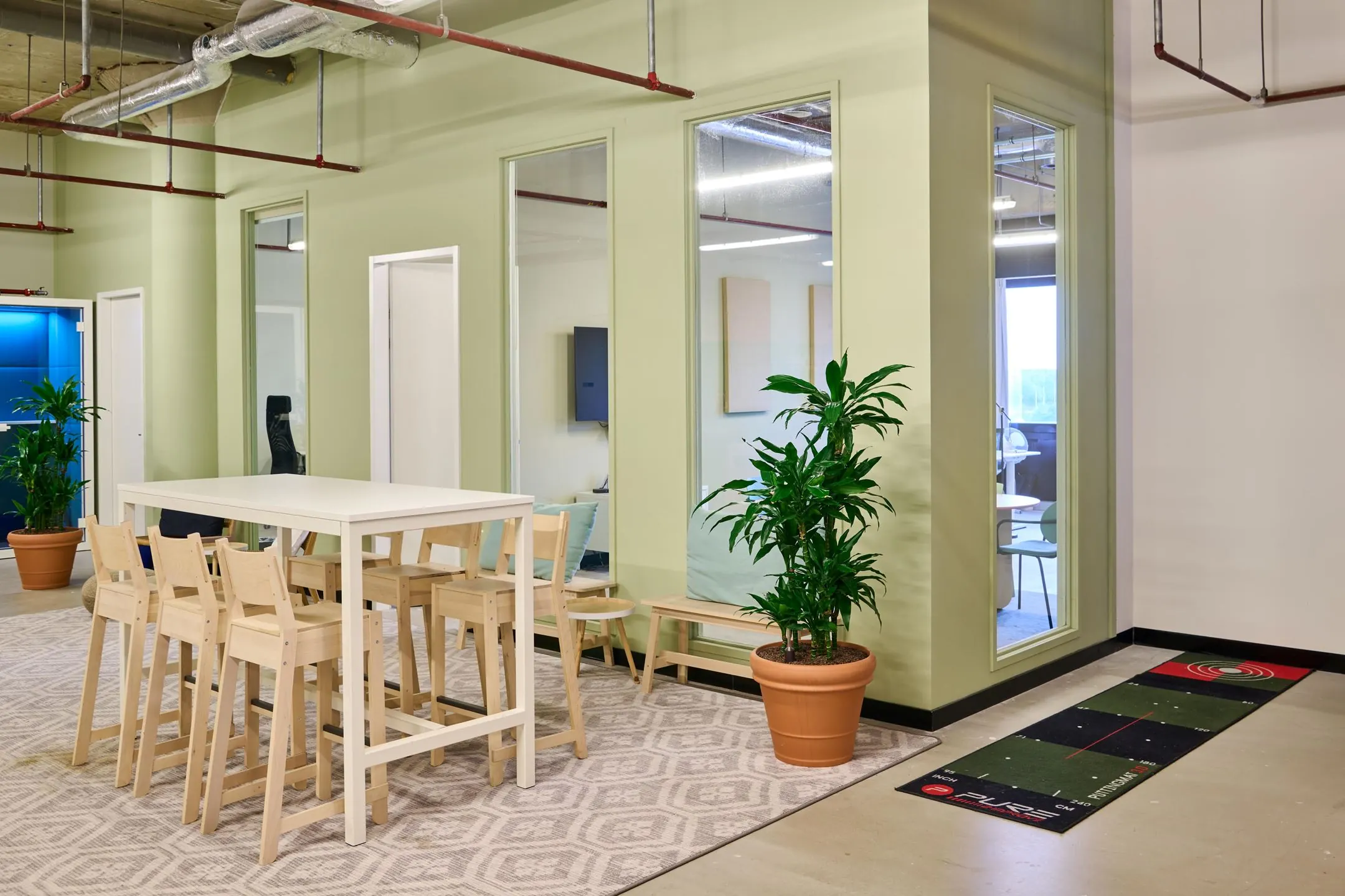 Moderne kantoorruimte aan de Johan Huizingalaan 763a met een hoge tafel, houten barkrukken, kamerplanten en een golfmat op de vloer.