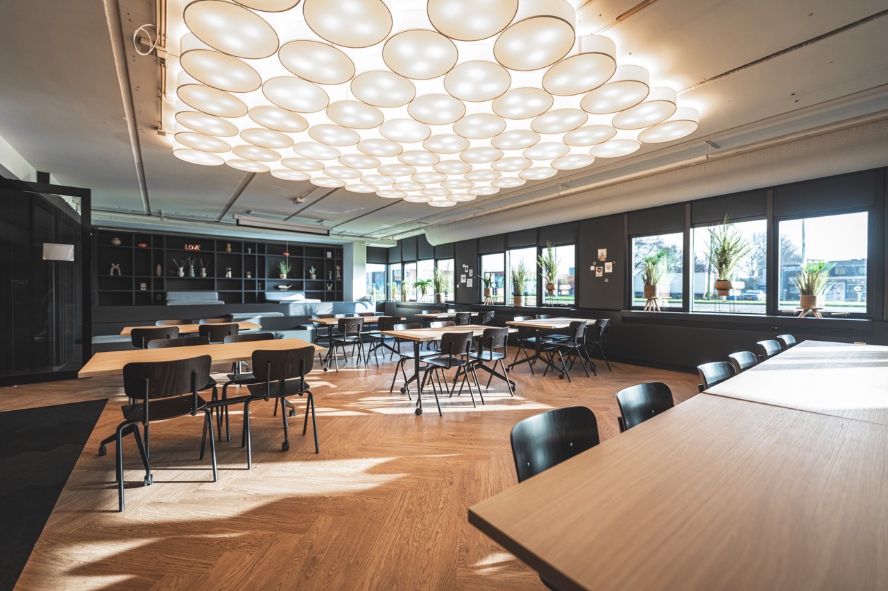 Een ruime, modern ingerichte vergader- of lunchruimte in de Jordaan met houten vloer, designverlichting en veel natuurlijk licht.