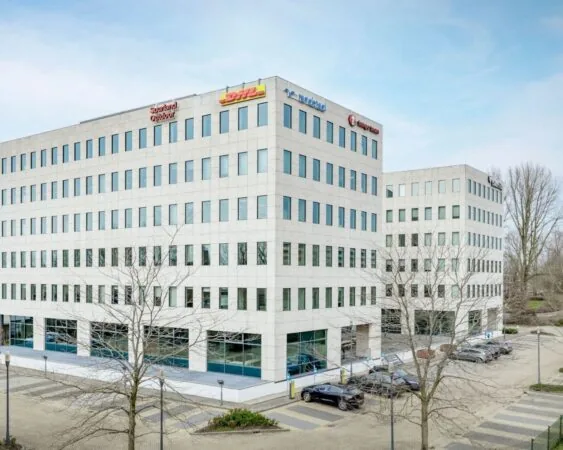 Modern kantoorgebouw aan de Anderlechtstraat 15 met diverse bedrijfslogo’s en aangrenzende parkeergelegenheid.