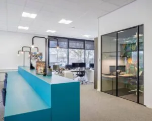 Moderne kantoorruimte op Anderlechtstraat 15 met werkplekken, glazen vergaderruimte en opvallende turquoise balie.