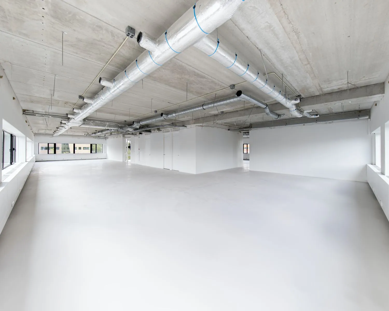 Lichte, moderne kantoorruimte te huur aan de Basicweg 12 in Amersfoort met zichtbare plafondinstallaties en grote ramen.