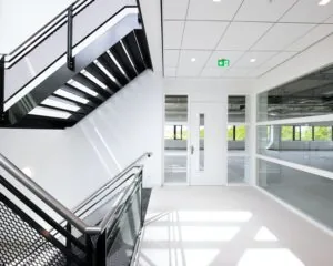 Moderne, lichte kantoorruimte met witte muren, grote ramen en een zwart metalen trap in het pand aan de Basicweg 12 in Amersfoort.