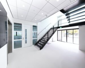 Moderne, lichte entree met zwarte trap en glazen deuren in kantoorpand aan de Basicweg 12 in Amersfoort.