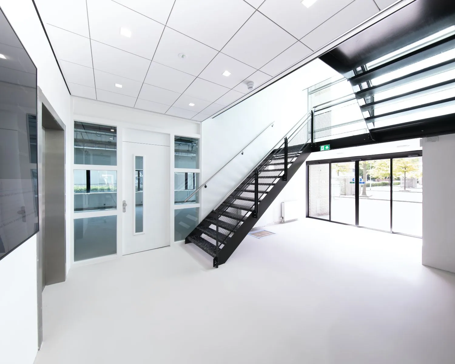 Moderne, lichte entree met zwarte trap en glazen deuren in kantoorpand aan de Basicweg 12 in Amersfoort.