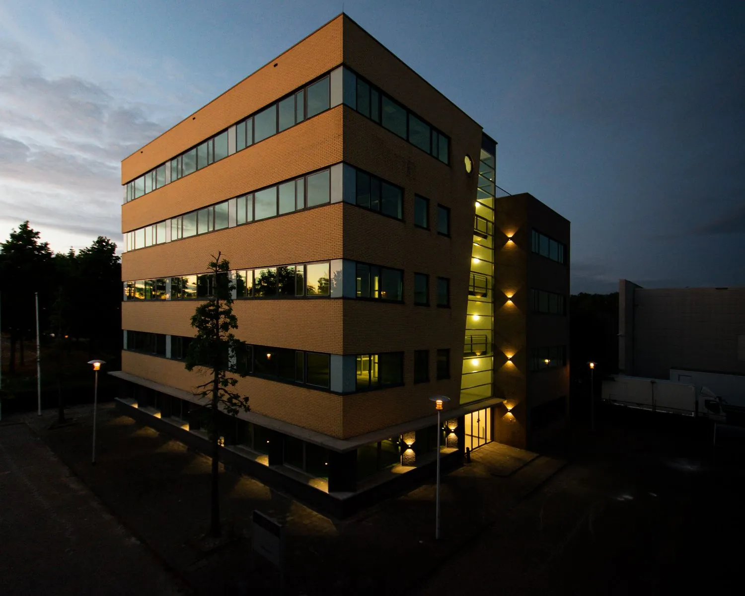 Verlicht kantoorgebouw aan de Basicweg 12 in Amersfoort tijdens schemering.