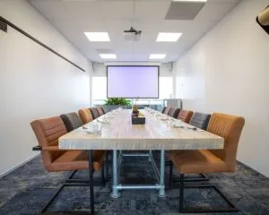 Vergaderruimte met lange houten tafel, moderne stoelen en een projector, gelegen aan de Boerhaavelaan 40.