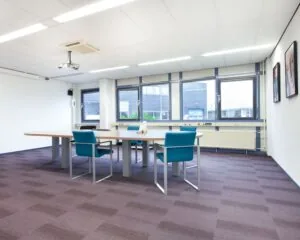 Moderne vergaderruimte met grote tafel, blauwe stoelen en veel daglicht in kantoorruimte aan Coenecoop 7.