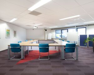 Vergaderruimte met U-vormige opstelling van tafels en blauwe stoelen in kantoorruimte Coenecoop 7-4.