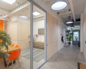 Moderne kantoorruimte aan de Corkstraat 46 in Rotterdam met glazen vergaderruimte, oranje stoelen en strakke industriële afwerking.