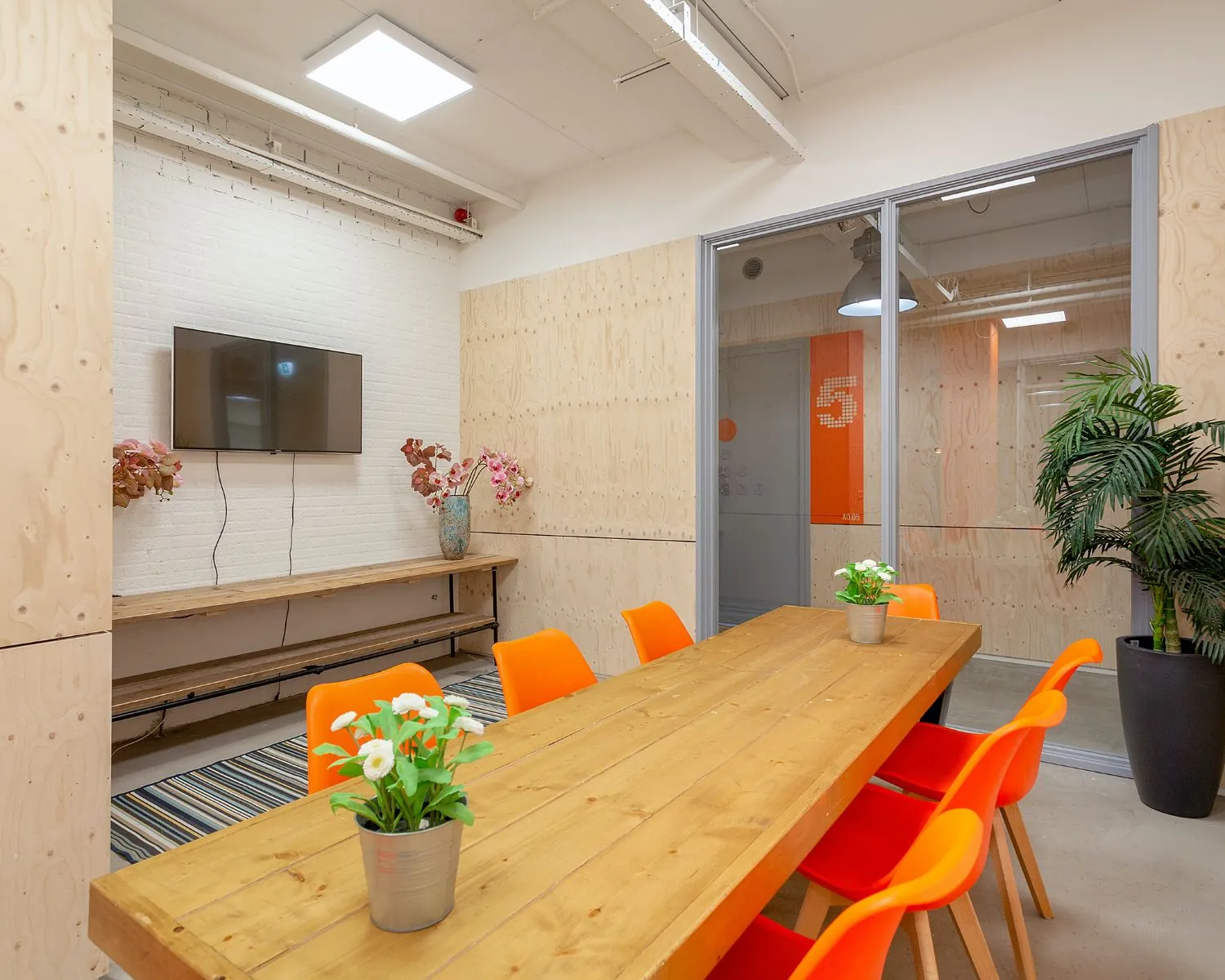 Moderne vergaderruimte in kantoor aan de Corkstraat 46 in Rotterdam met houten tafel, oranje stoelen en een televisie aan de muur.