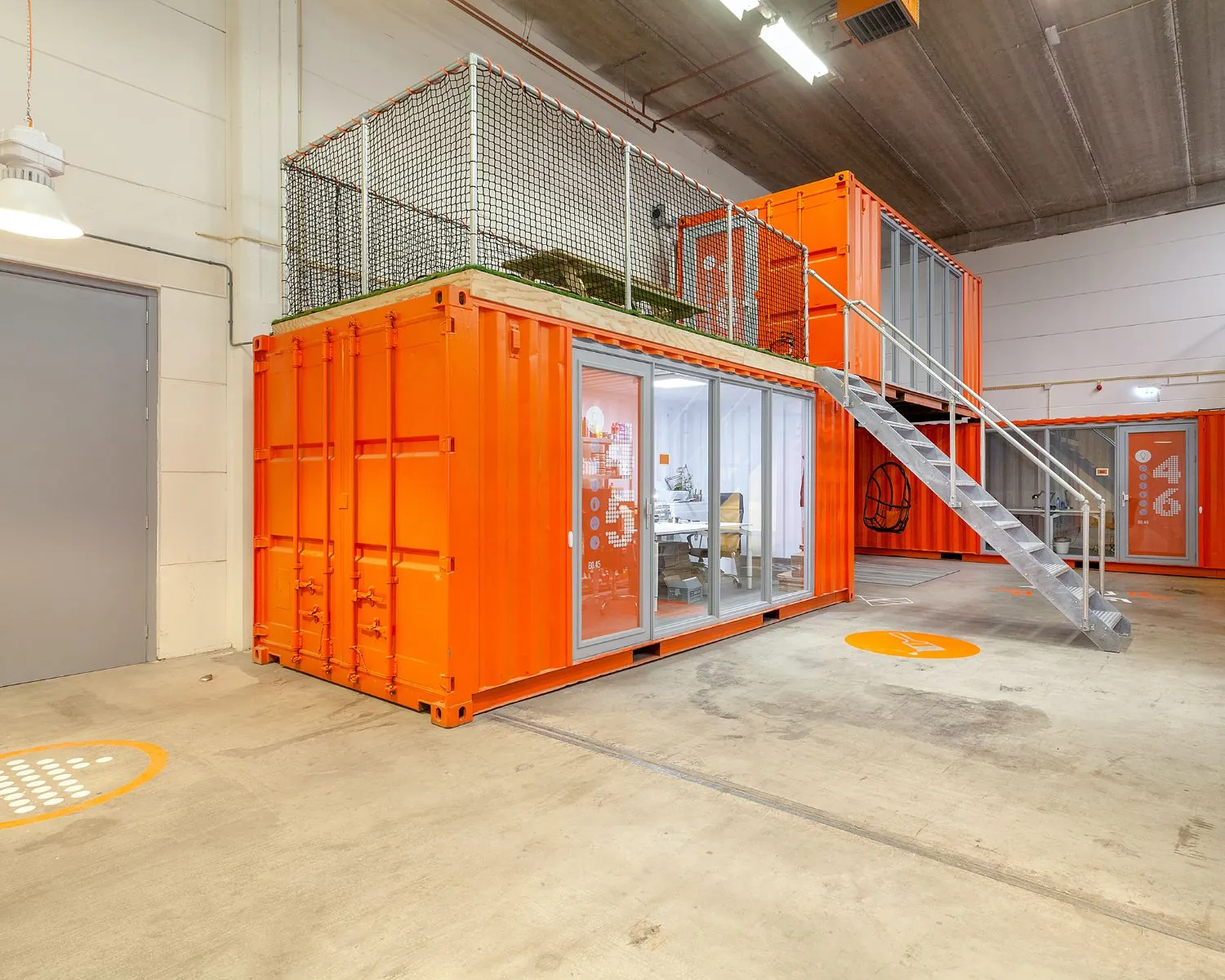 Moderne kantoorruimte in Rotterdam opgebouwd uit feloranje zeecontainers met glazen wanden en een metalen trap.
