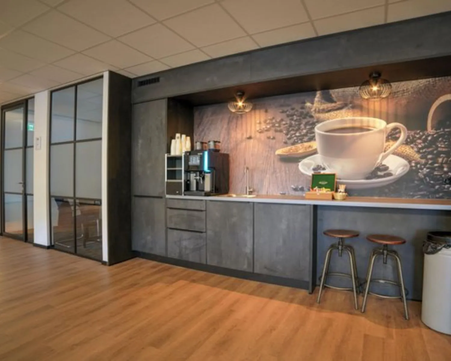 Moderne kantoorruimte aan de Cypresbaan 3 met een koffiehoek en barkrukken tegen een wand met een grote afbeelding van een koffiekop.